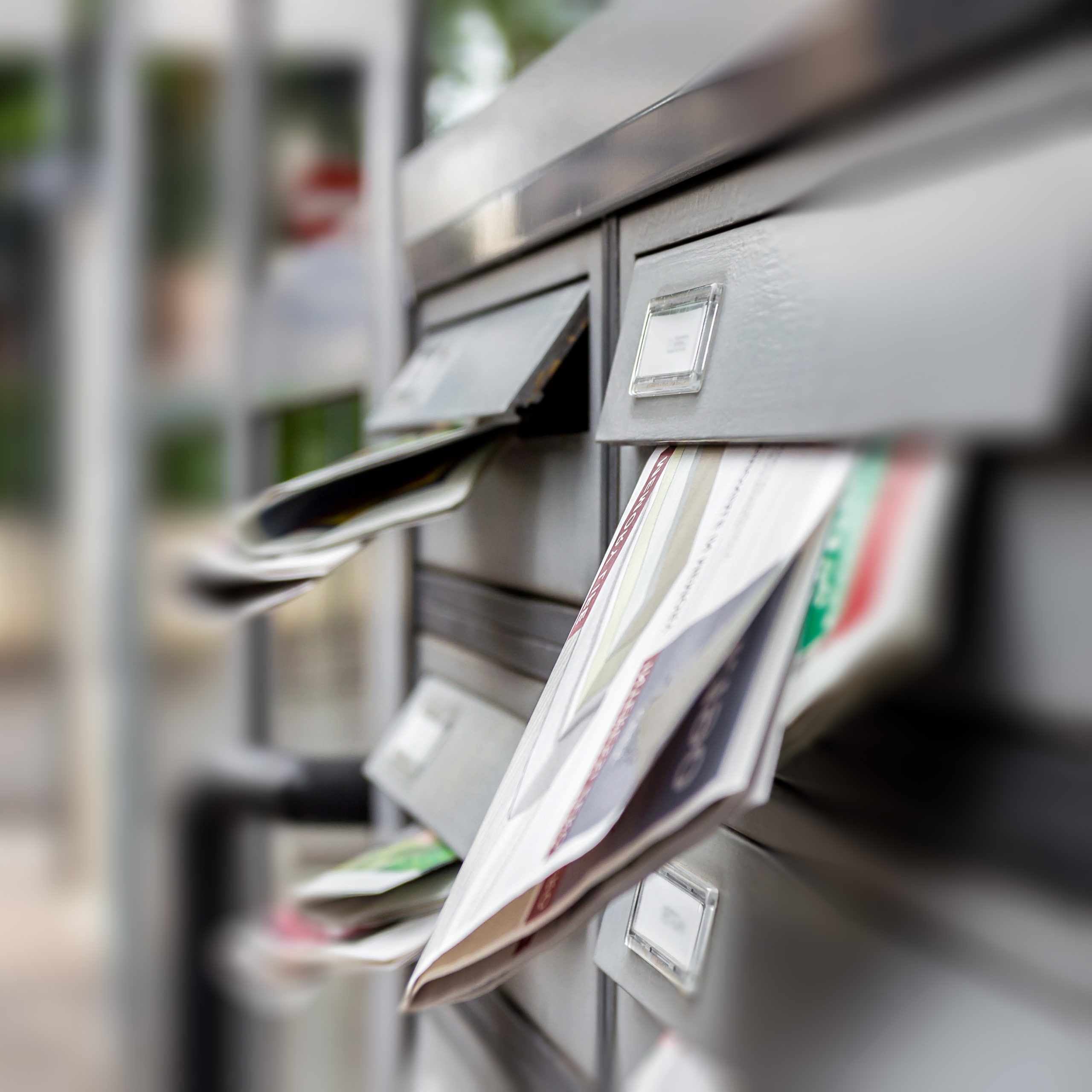 Mailbox full of junk of adverstising brochures outside apartment block. Defocused blurry background.